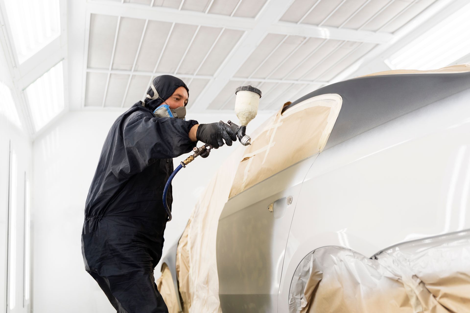 A person in protective gear spray painting a car in a well-lit workshop.