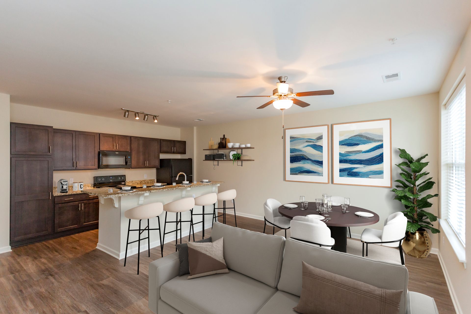 Modern apartment living room with a brown couch, kitchen island with stools, and a round dining table with four chairs.