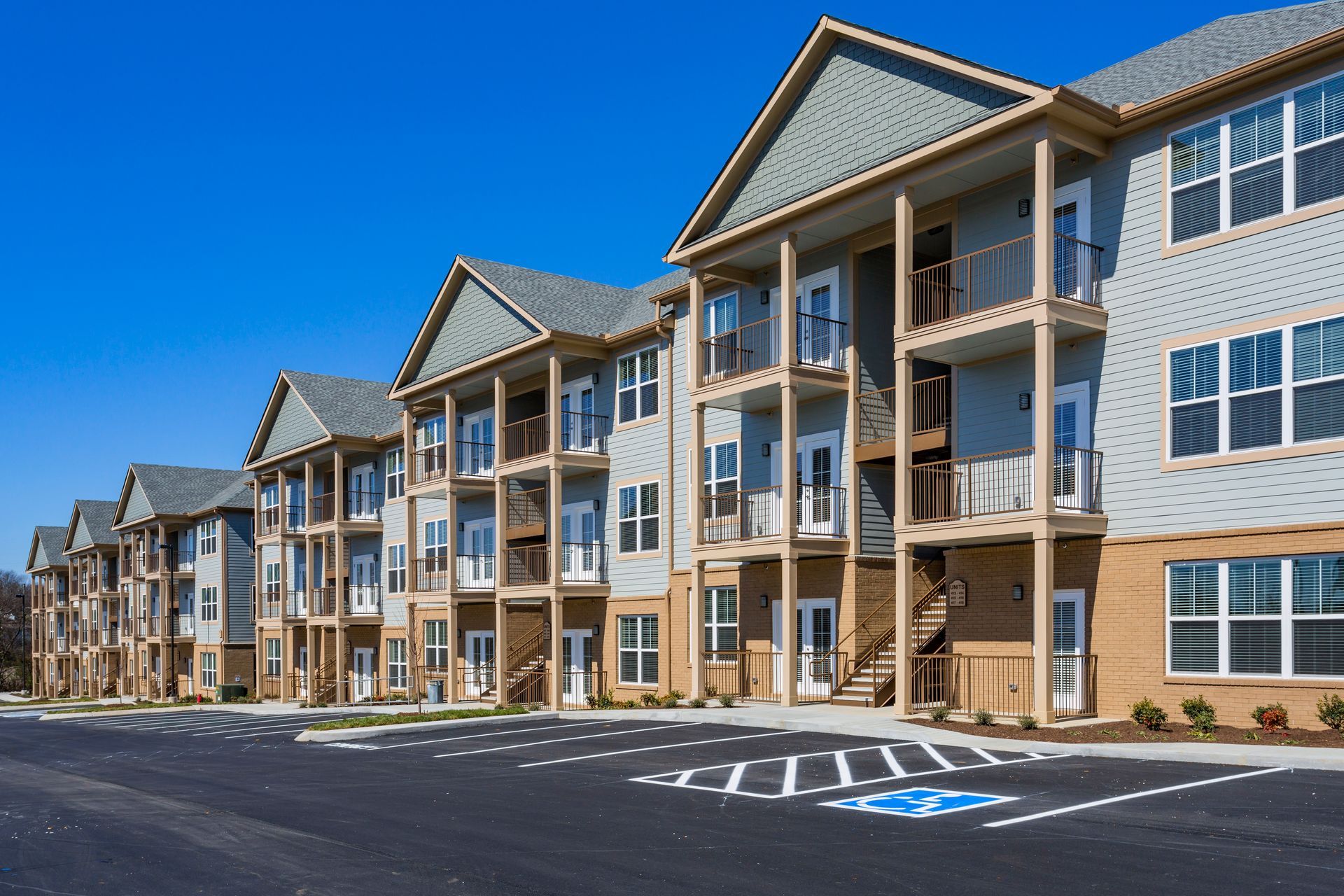 A multi-story apartment complex with gray siding, beige brick, and balconies against a clear blue sky.