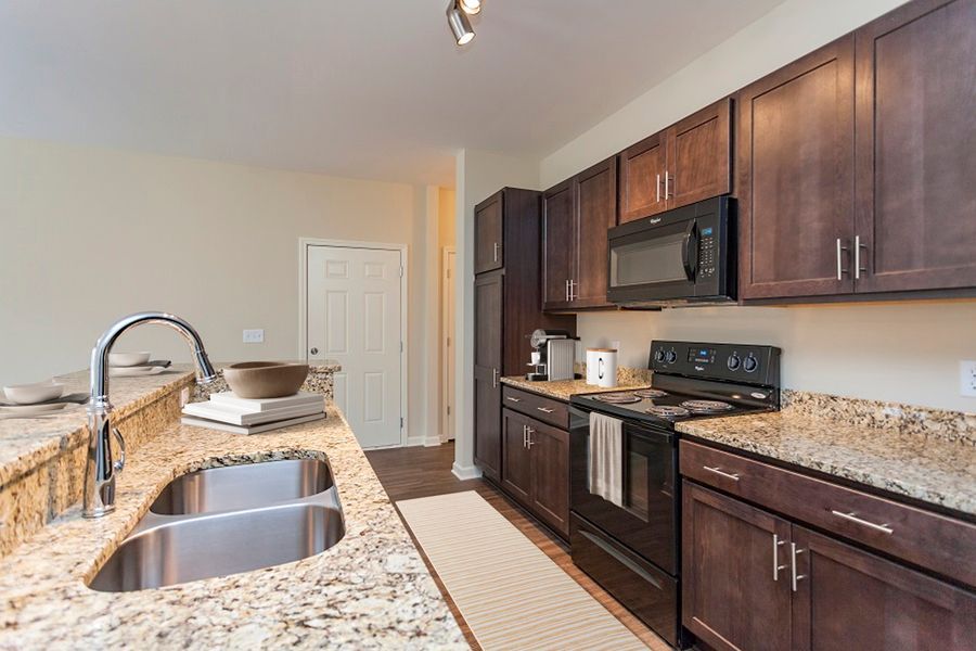 A modern kitchen featuring dark wood cabinets, speckled granite countertops, a stainless steel sink, and black appliances.