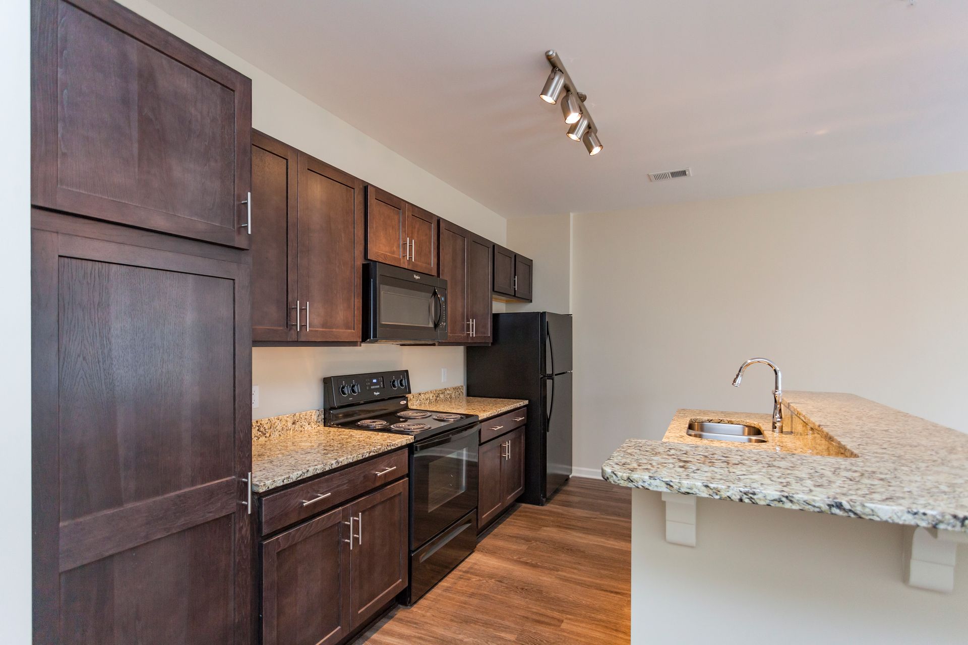 A kitchen featuring dark wood cabinets, granite countertops, stainless steel appliances, and a breakfast bar.