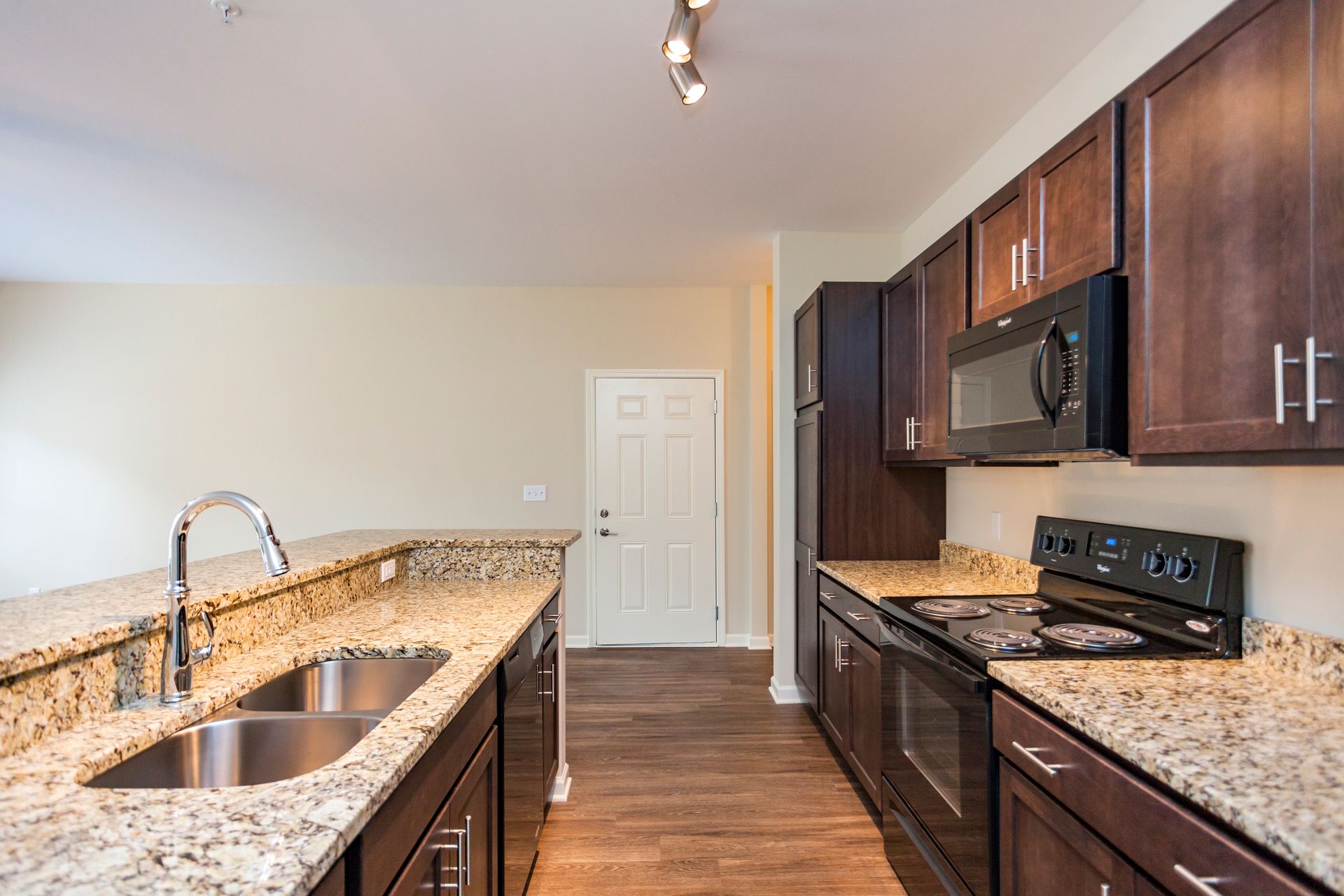 A kitchen with dark wood cabinets, granite countertops, a stainless steel sink, and black appliances.