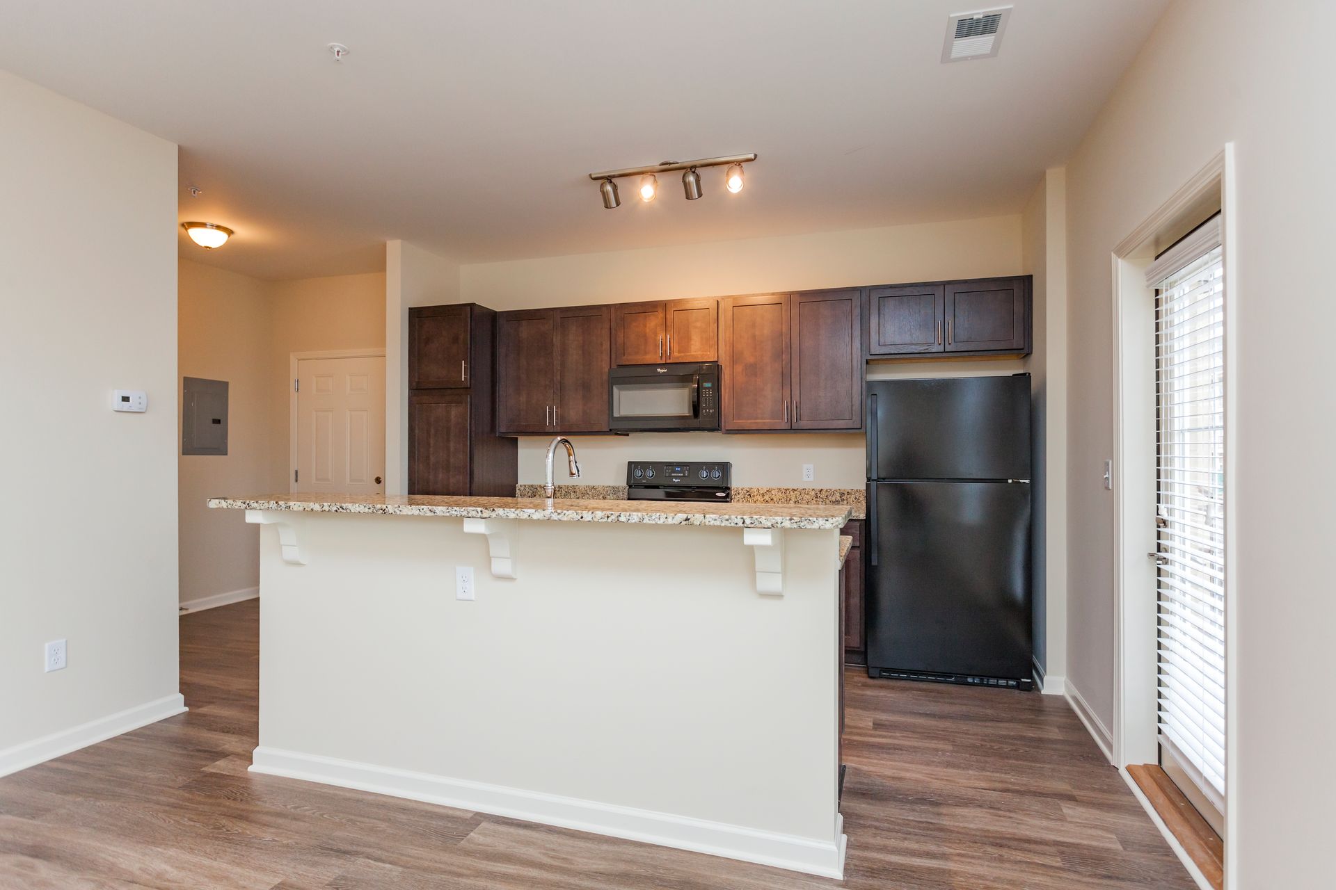 A kitchen with brown cabinets, granite countertops, and a black refrigerator, featuring a central breakfast bar island.