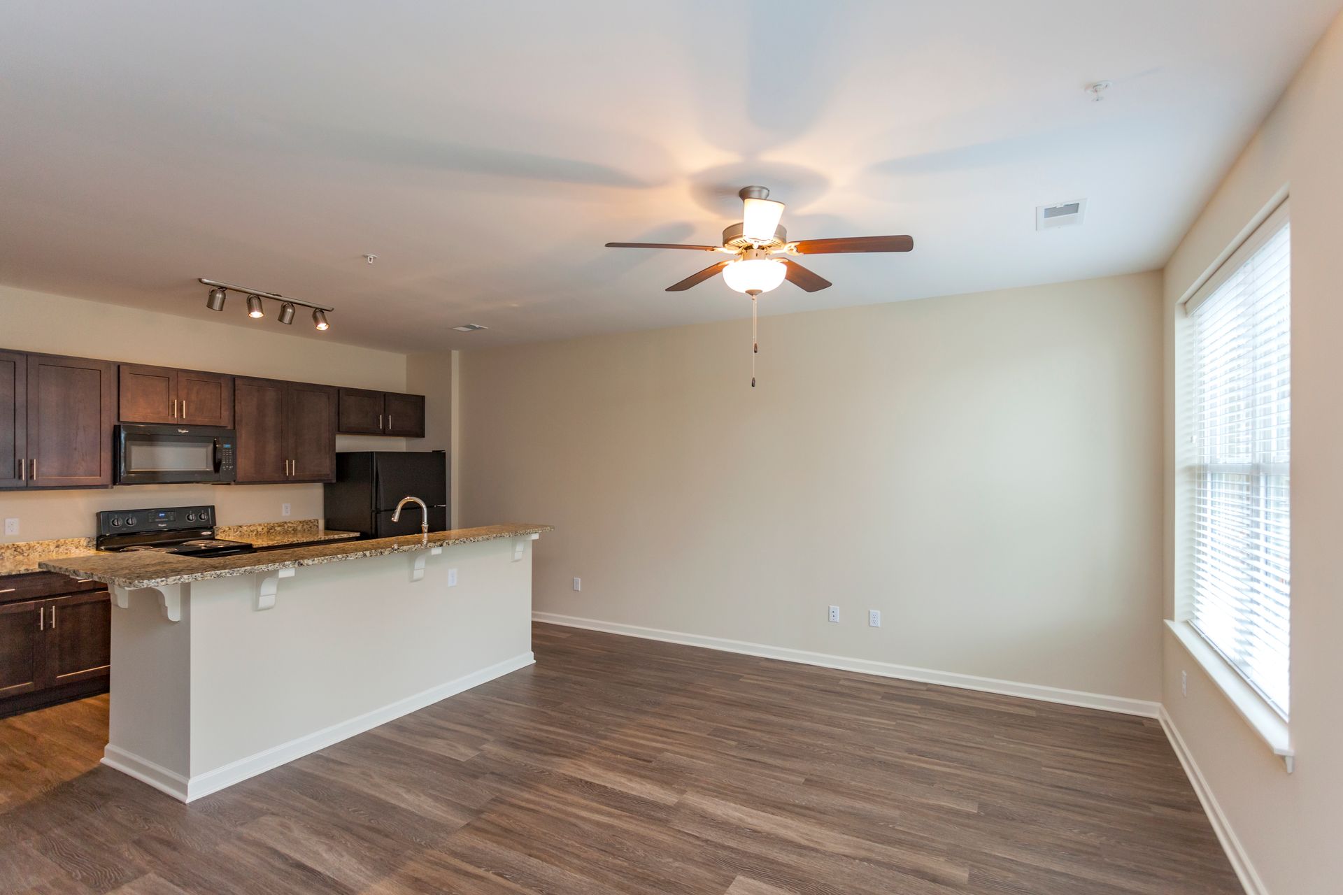 An open-concept living area with dark wood floors, a breakfast bar, dark wood kitchen cabinets, and a ceiling fan.