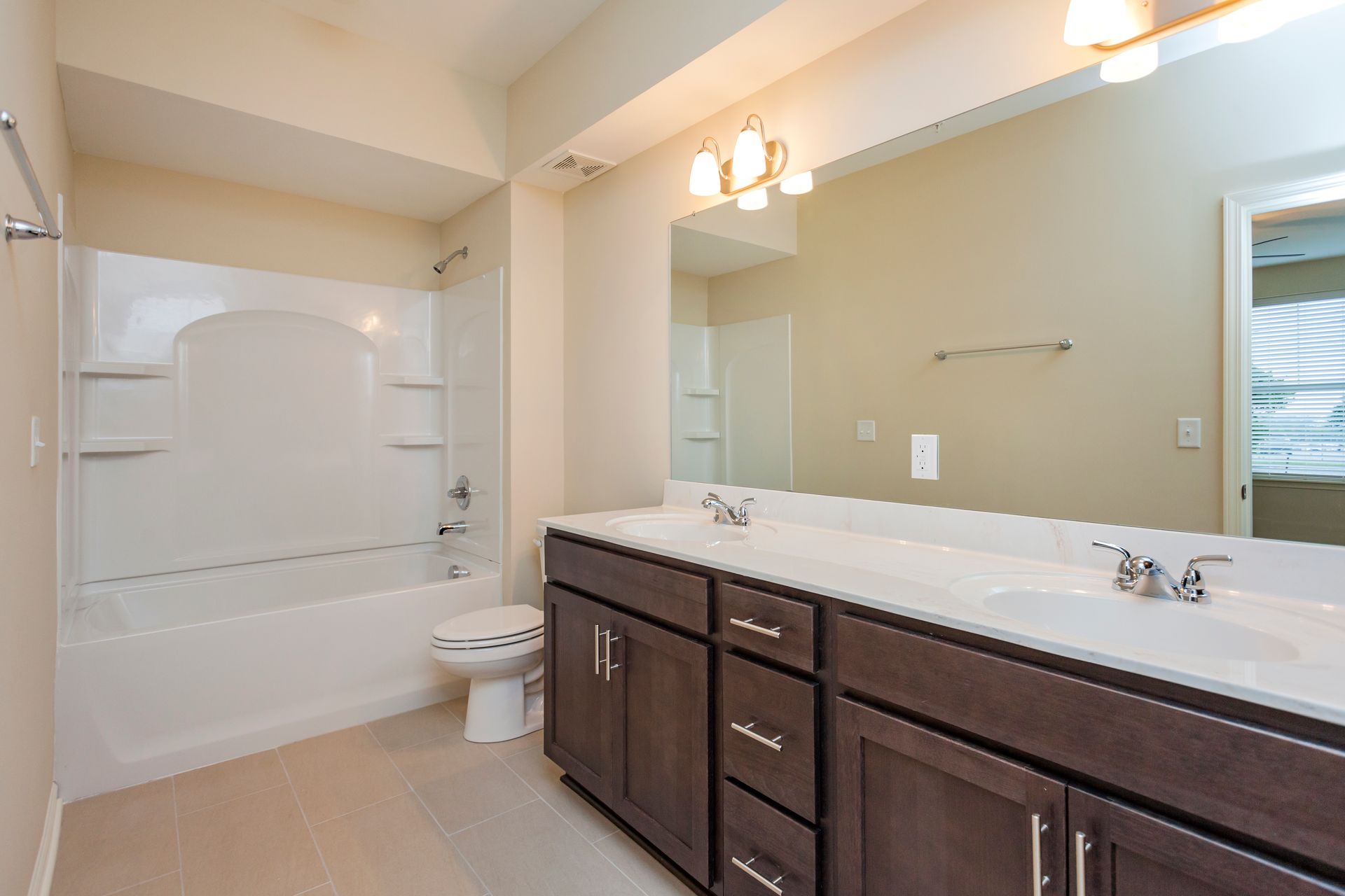 A bathroom with a white tub and shower combo, a dark wood double vanity with a mirror, and a white toilet.