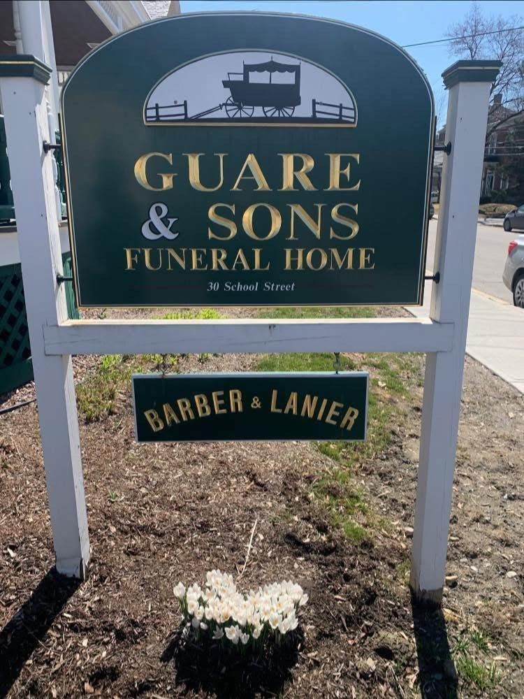 Two men holding a sign for Barber & Lanier Funeral Home outside the building.