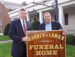 Two men holding a sign for Barber & Lanier Funeral Home outside the building.