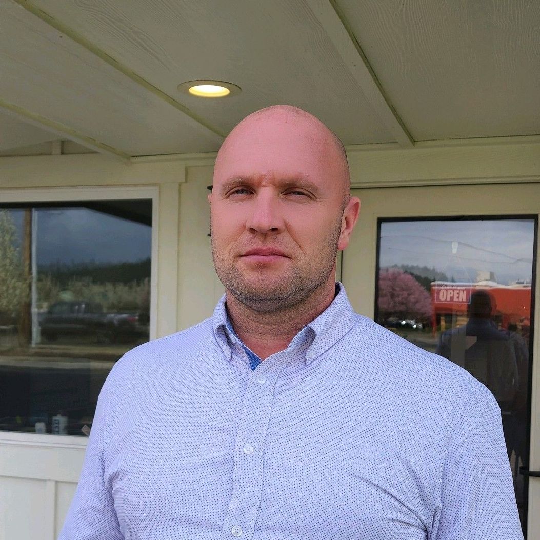 A man in a light blue shirt stands in front of a building.