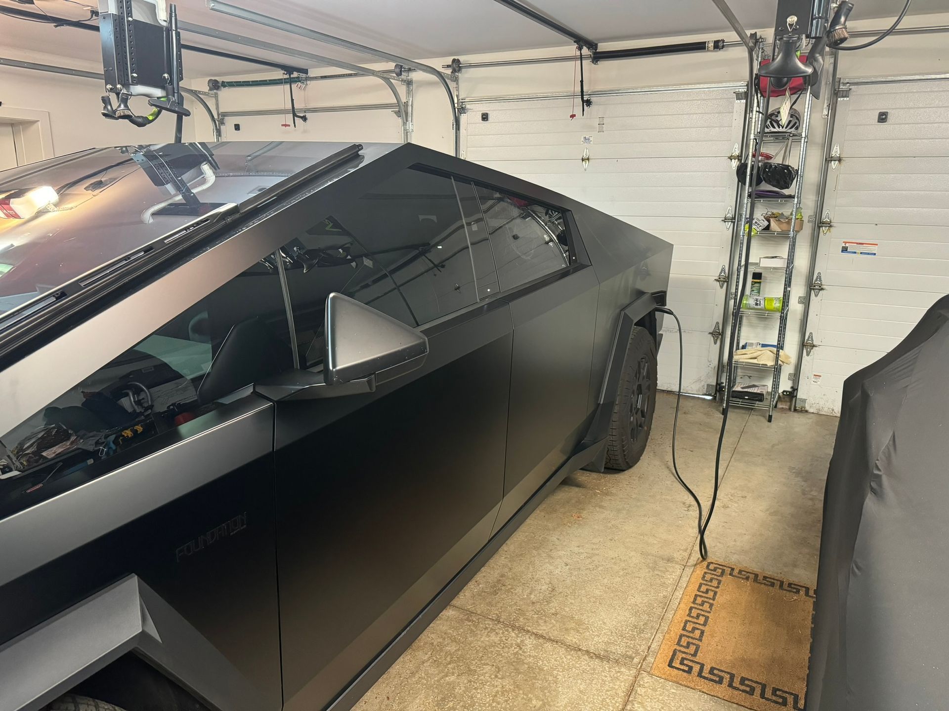 A Cybertruck is parked in a garage, plugged into a charger.