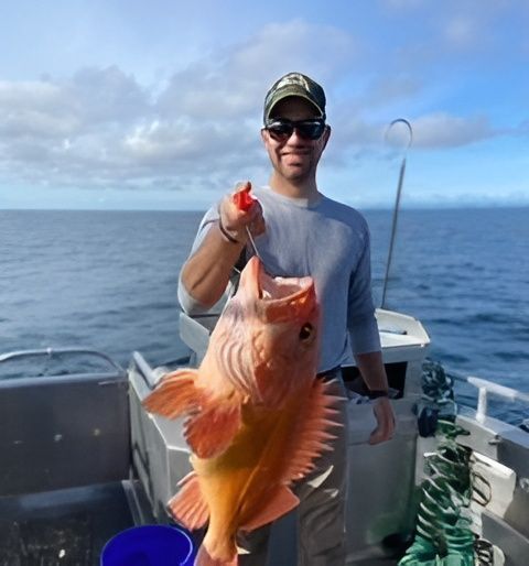 A person on a boat holds a large, orange fish with visible teeth using a red grip.