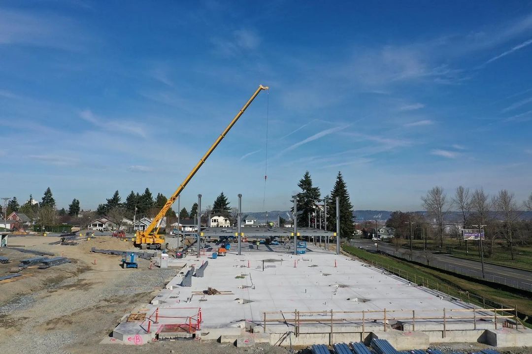 Construction site with yellow crane over large concrete area, metal beams and materials scattered.