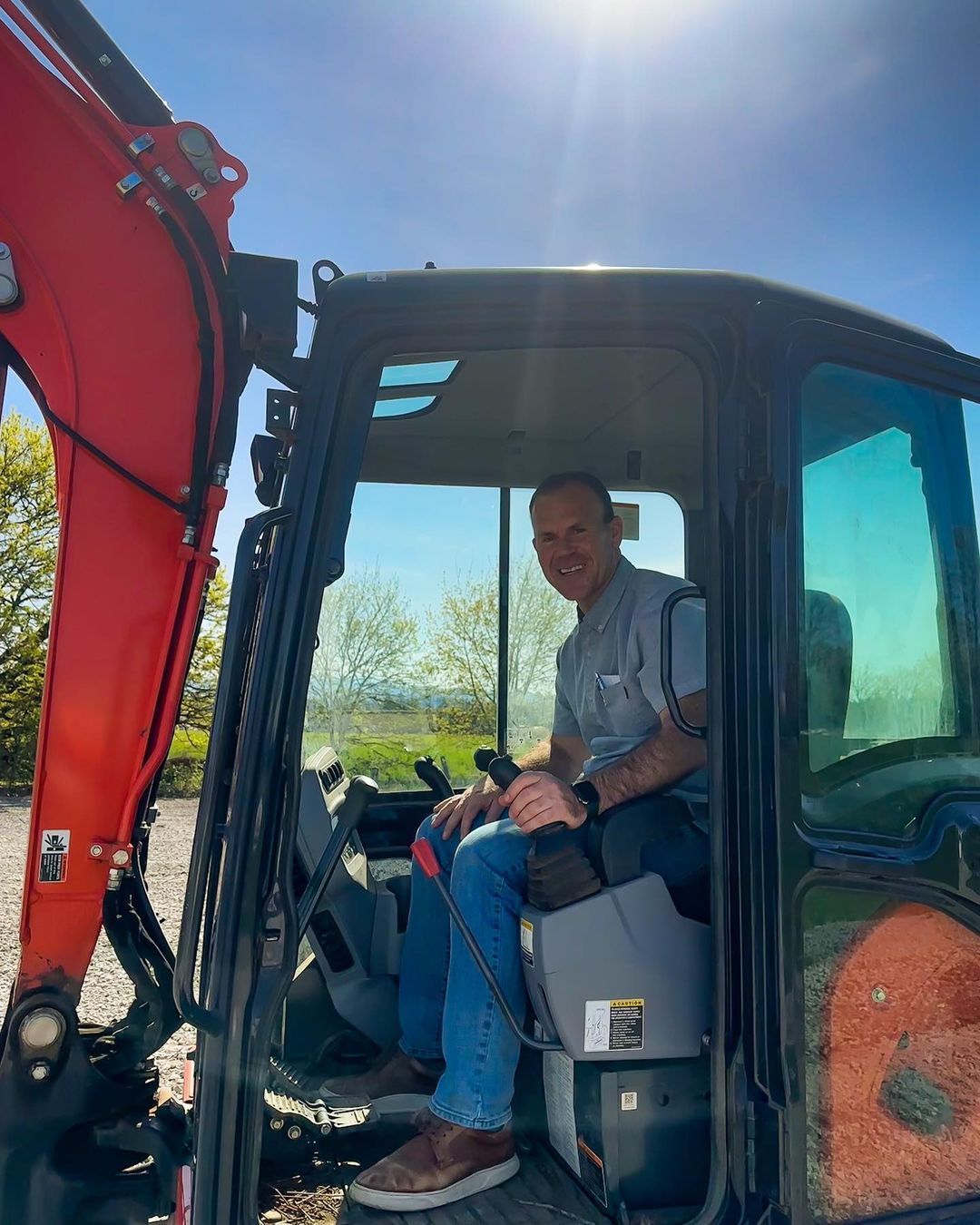 A person sitting inside a small excavator, holding the controls with one hand.