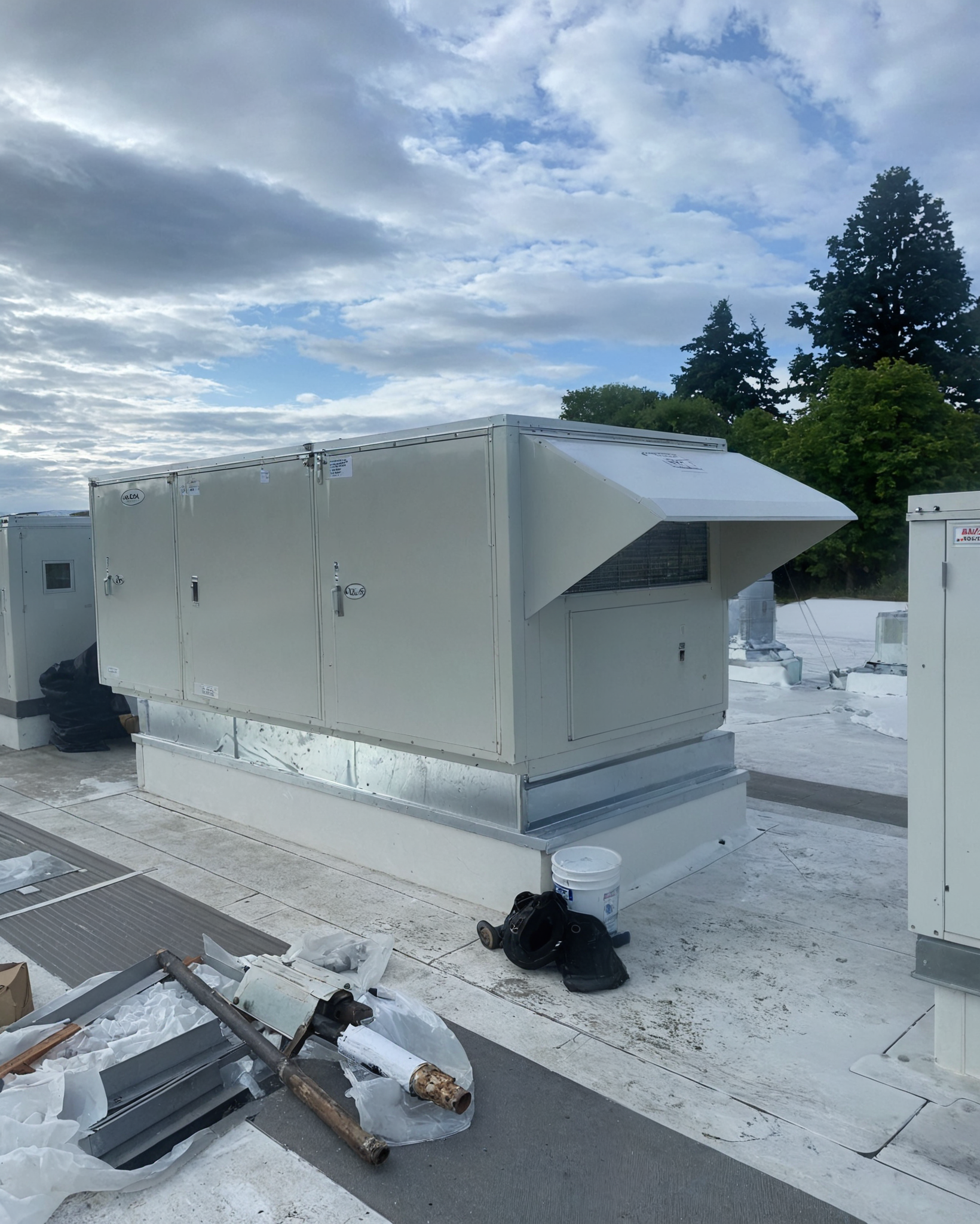 Crane lifting large industrial unit outdoors, two workers in yellow safety vests.