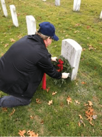 Person with red scraf placing wreath on Military Grave marker