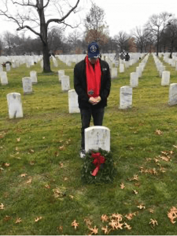 Person with red scraf placing wreath on Military Grave marker