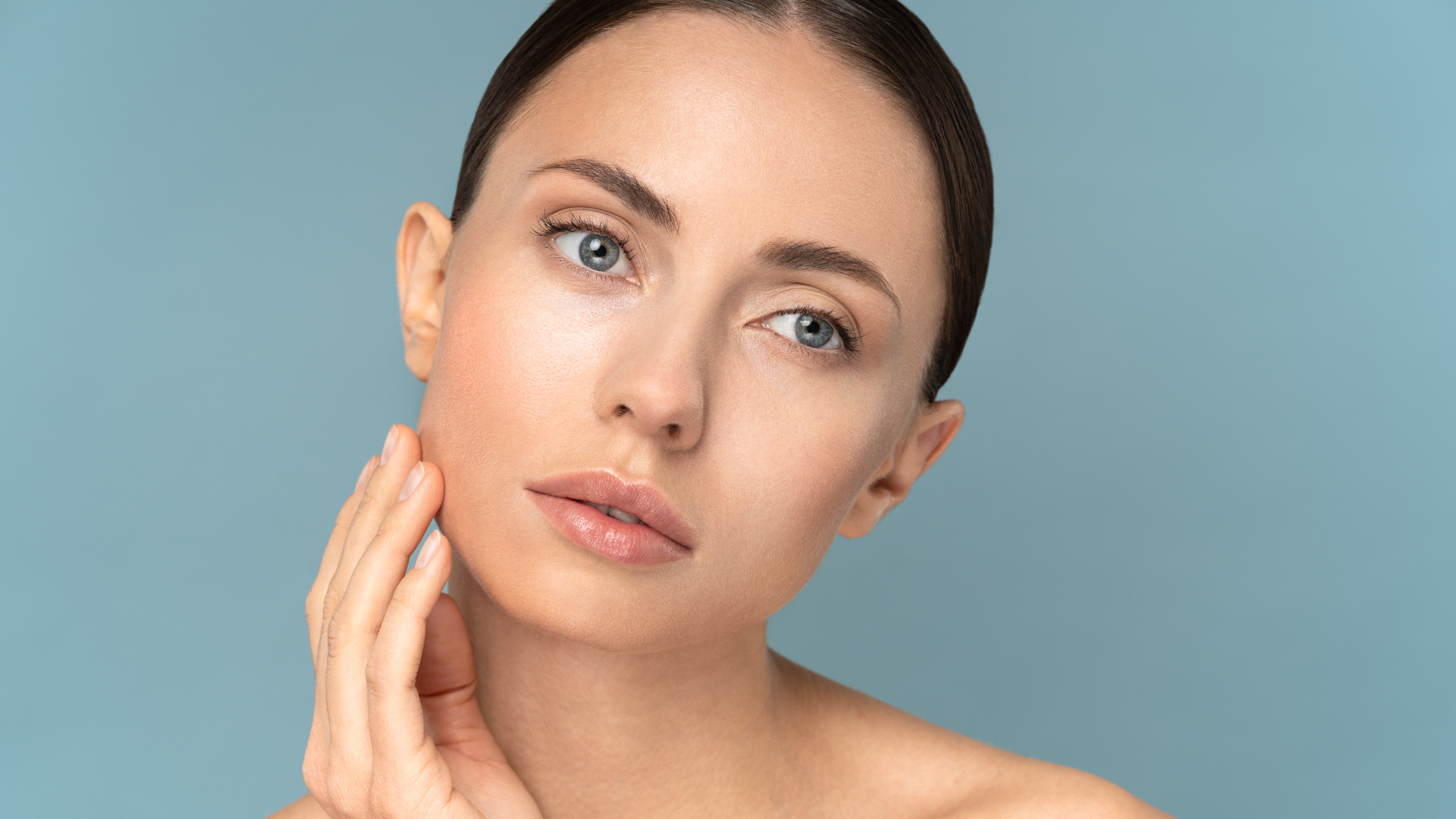 A woman is touching her face with her hand and looking at the camera.