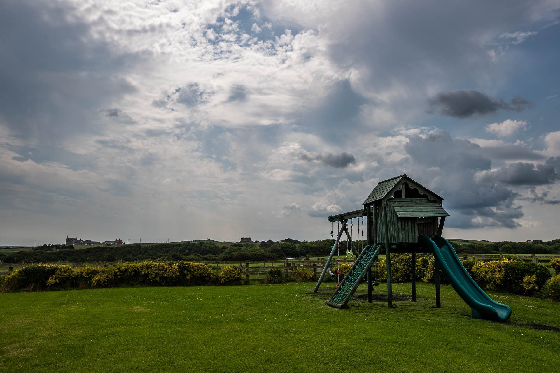 Playground with slide and swings in a grassy yard under a cloudy sky.