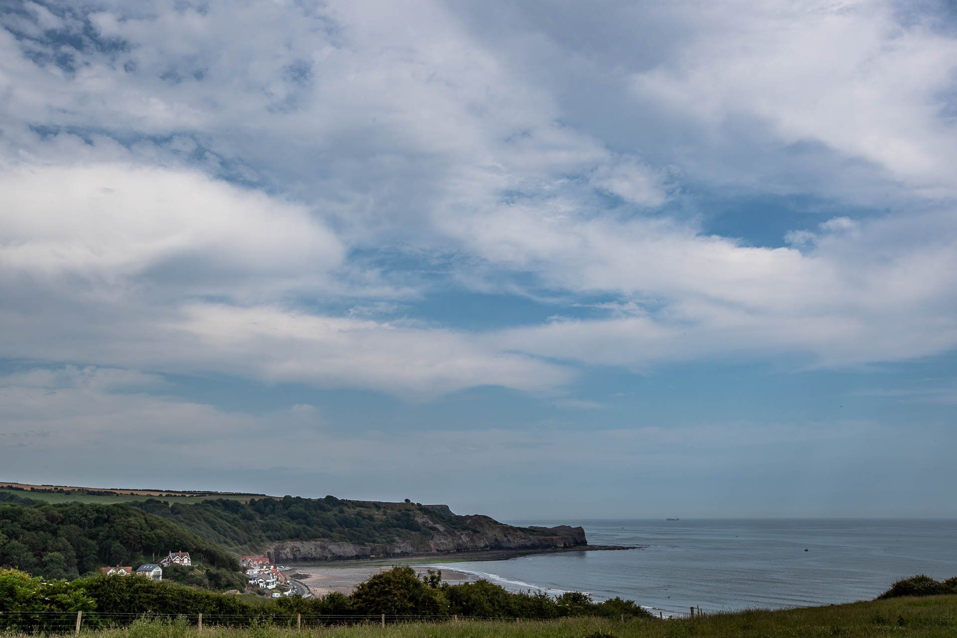 Coastal view with beach, cliffside buildings, and cloudy sky over water.