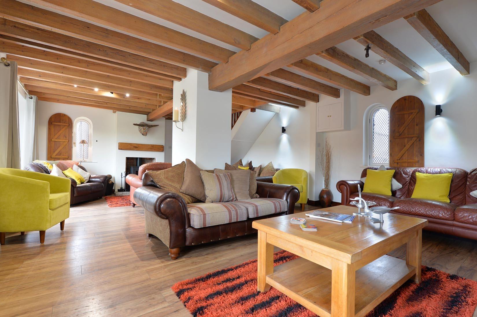 Living room with wood beams, leather sofas, yellow chairs, and a fireplace.