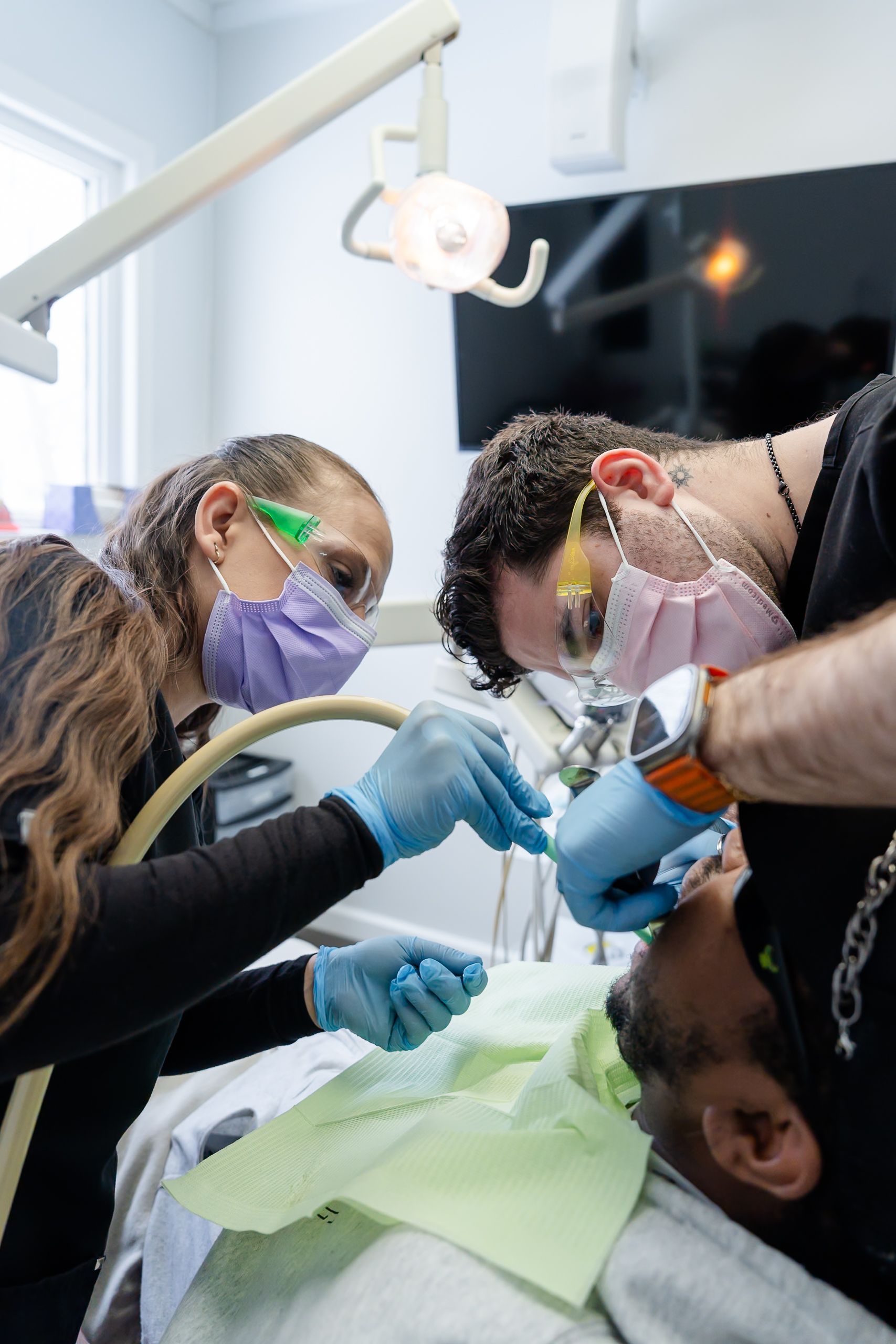 Dentist and assistant treating patient in a dental clinic. They wear masks and gloves.
