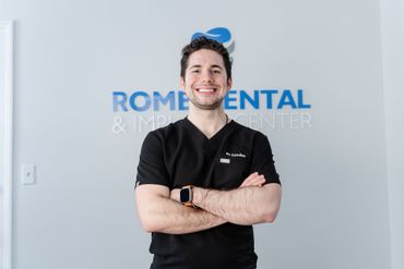 Man in black scrubs smiles with arms crossed in front of 