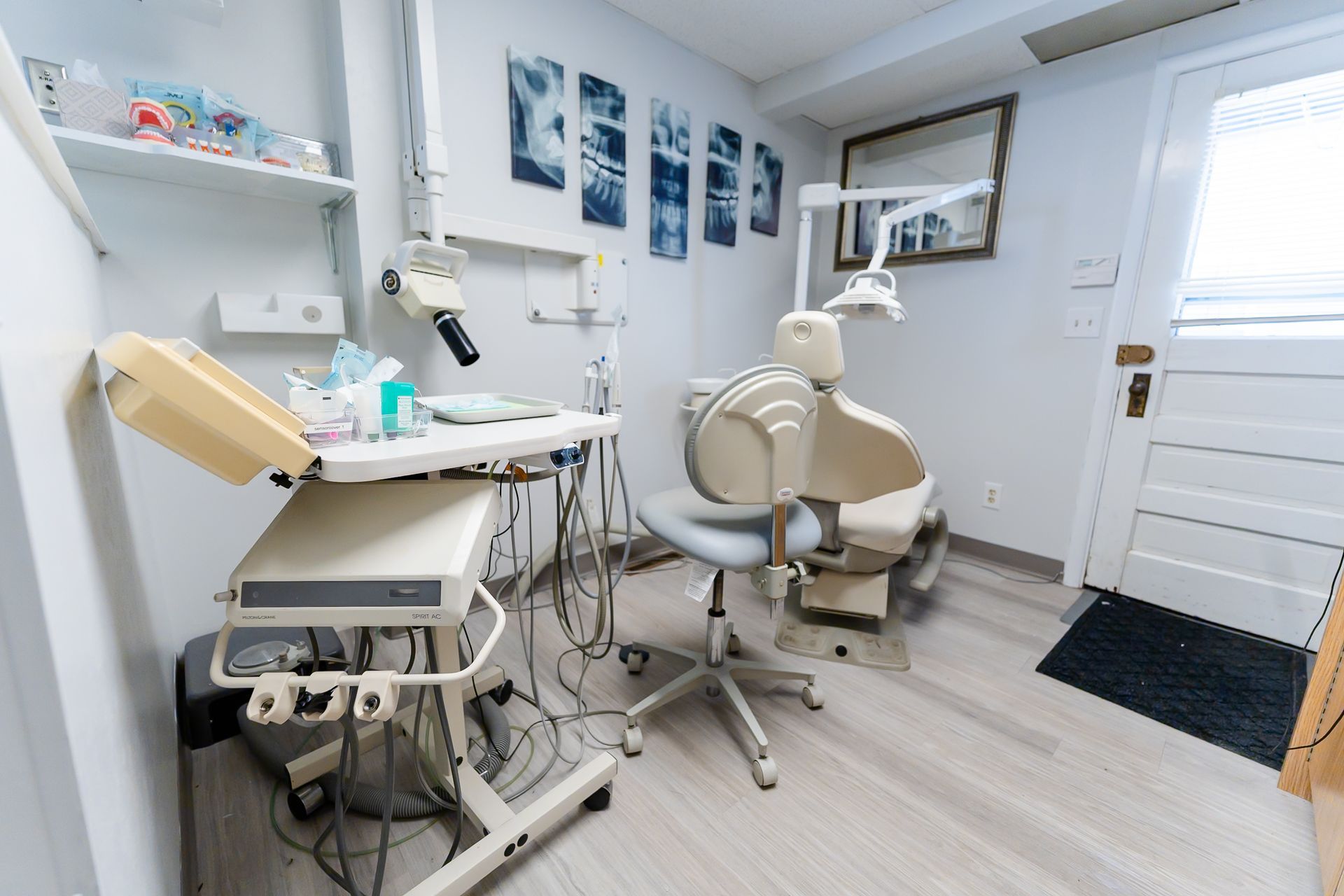 Dental office room: dental chair, equipment, X-ray images on wall, white and neutral colors.
