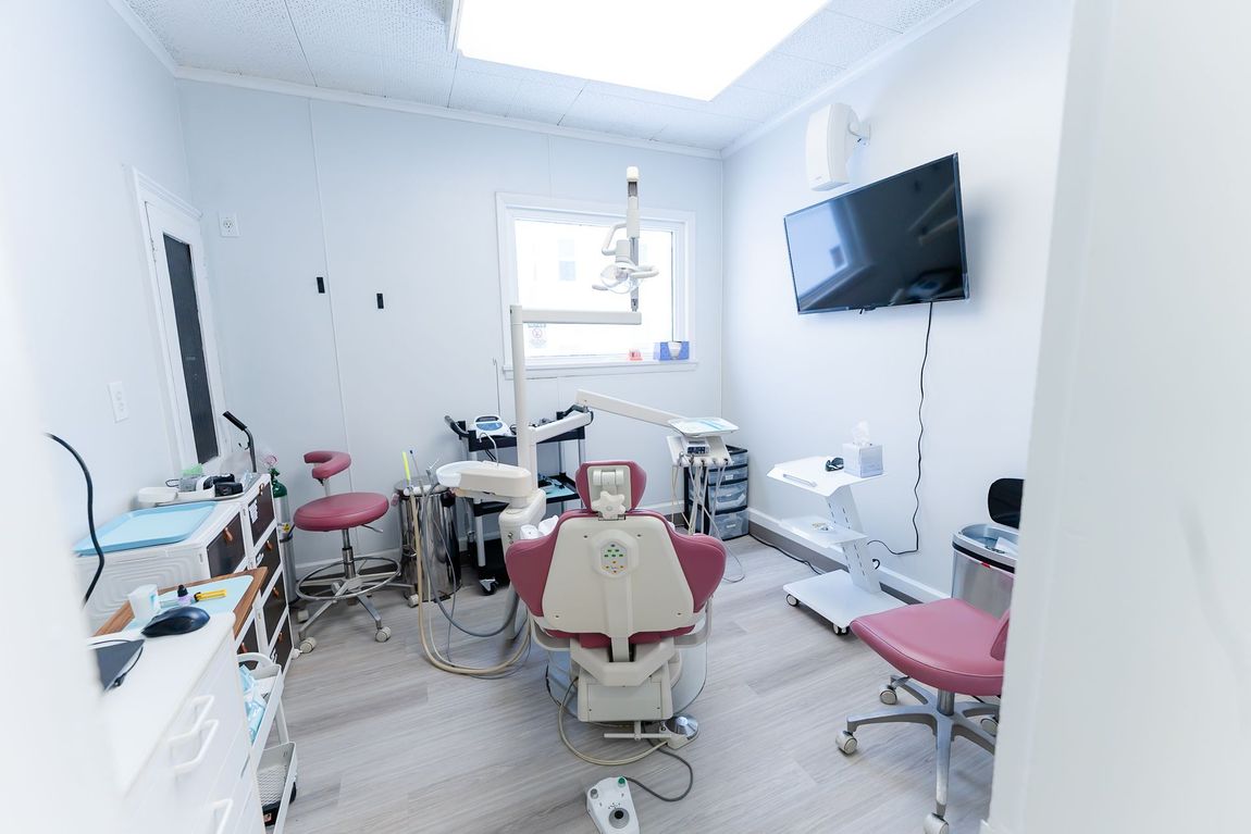 Dental examination room, white and pink, with chair, equipment, and a TV.