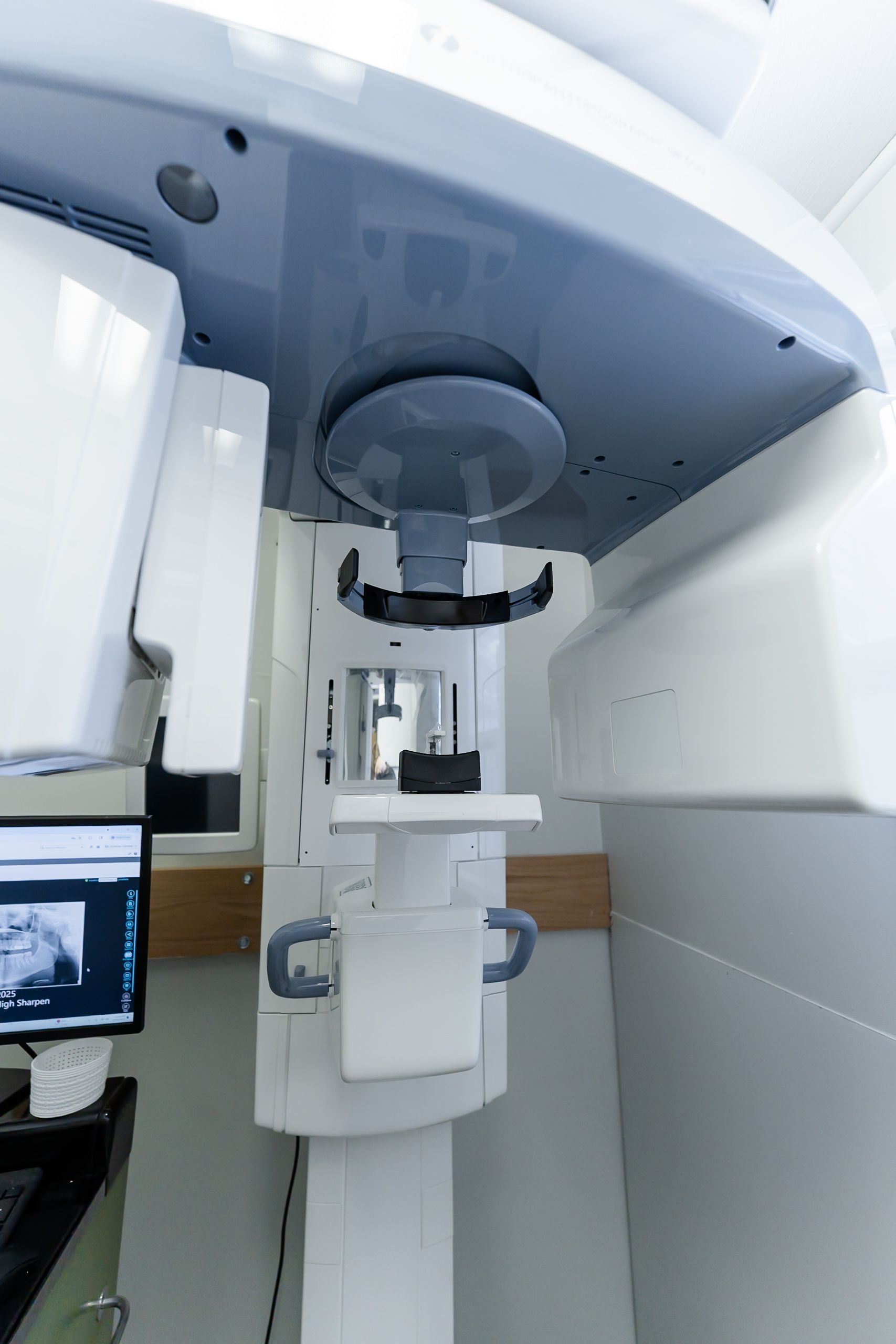 Dental panoramic X-ray machine. White and gray, a patient's head rests on the chin support, computer display nearby.