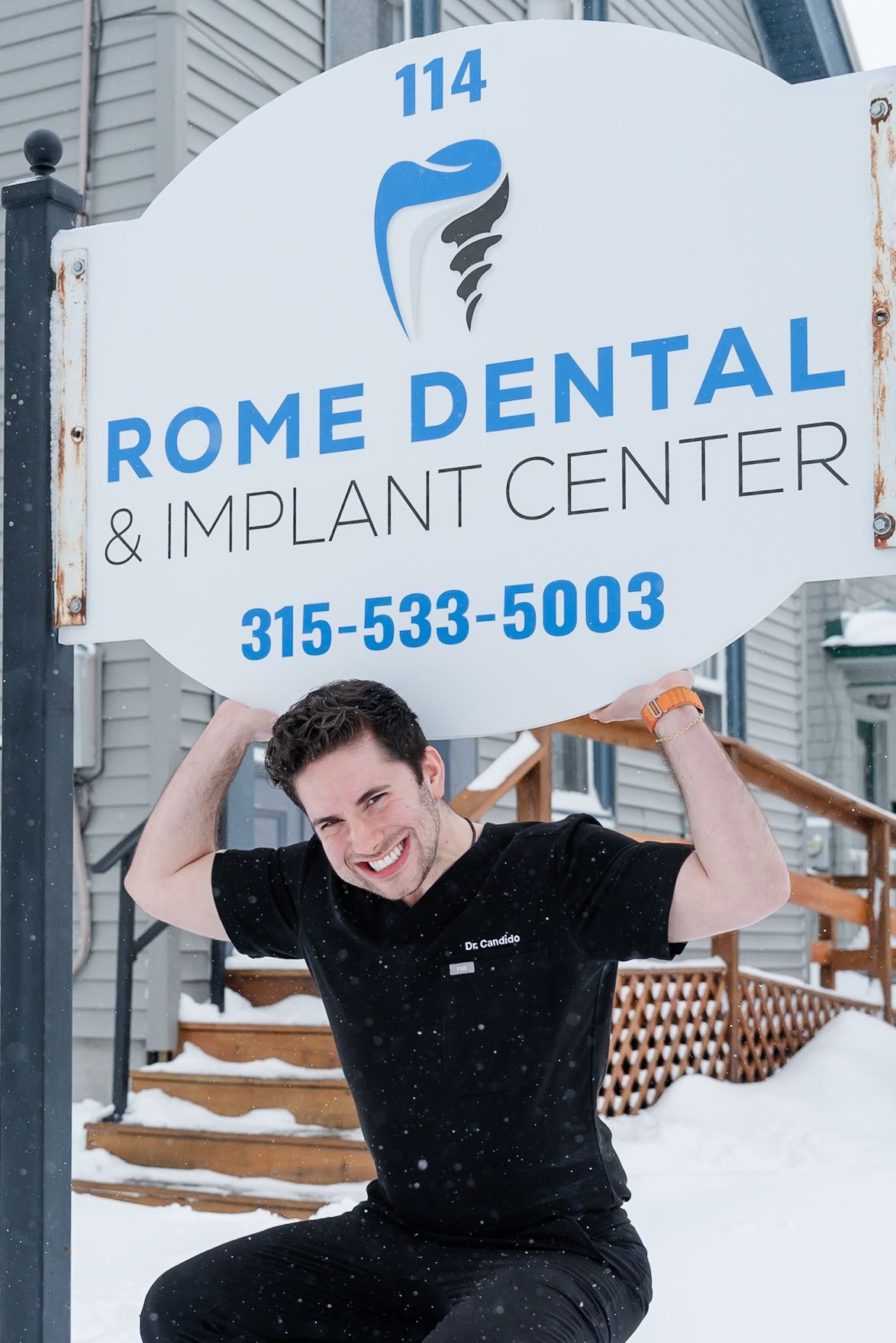 Man holding dental clinic sign, smiling outside in the snow.