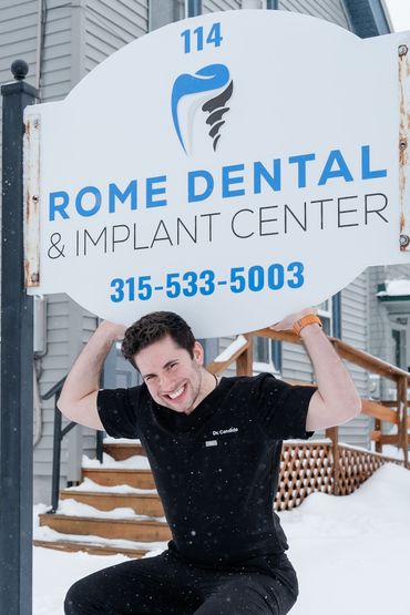 Man holding dental clinic sign, smiling outside in the snow.