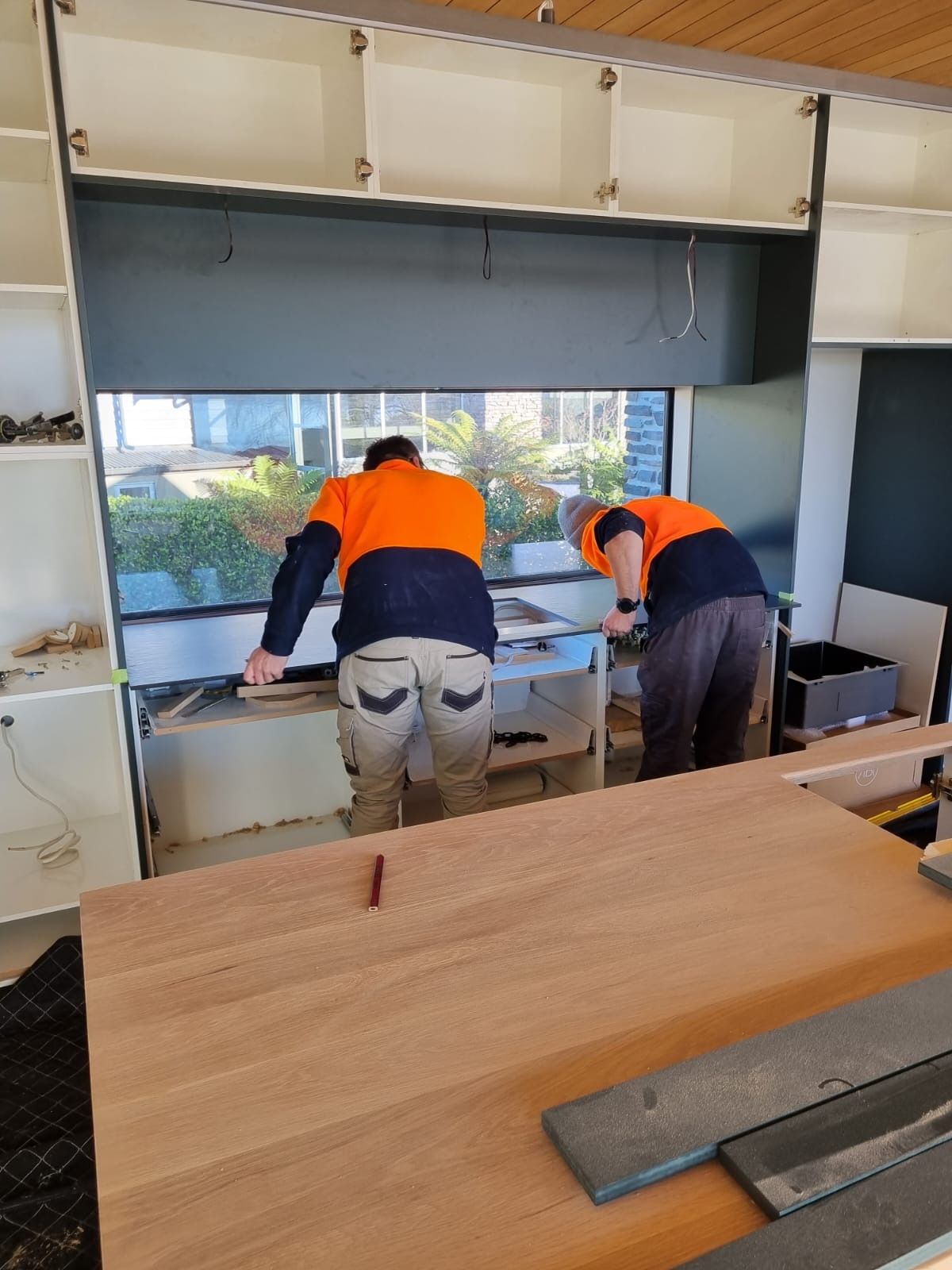 Two men are working on a wooden table in a kitchen.