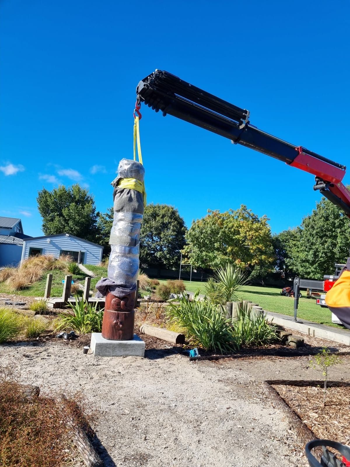 A large statue is being lifted by a crane in a park.