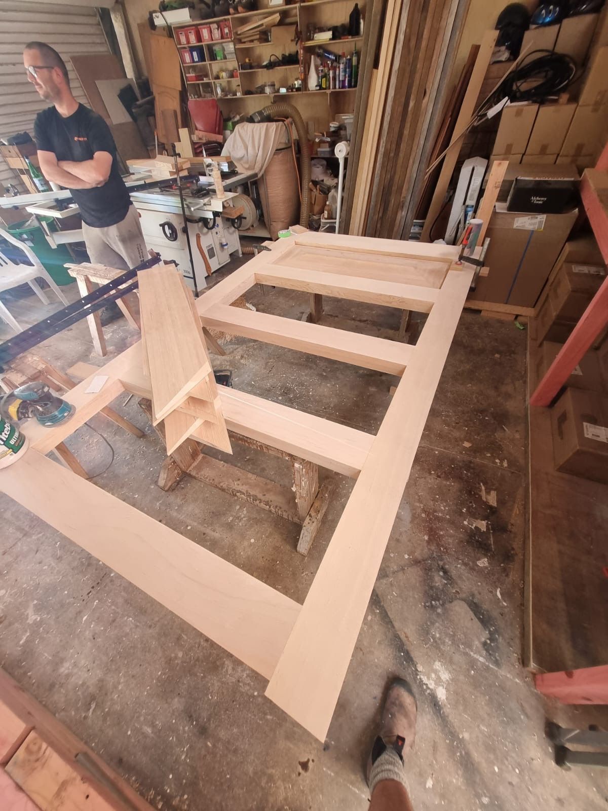 A man is standing next to a large piece of wood in a workshop.