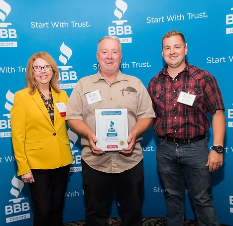 Three people pose in front of a blue BBB
