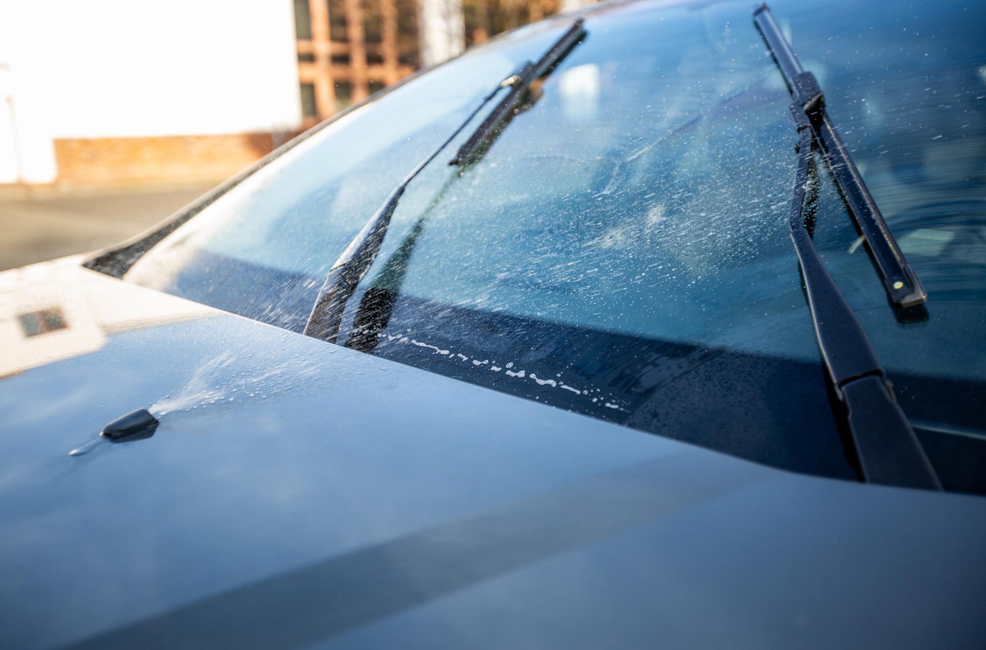 Car windshield with wipers, covered in water droplets.