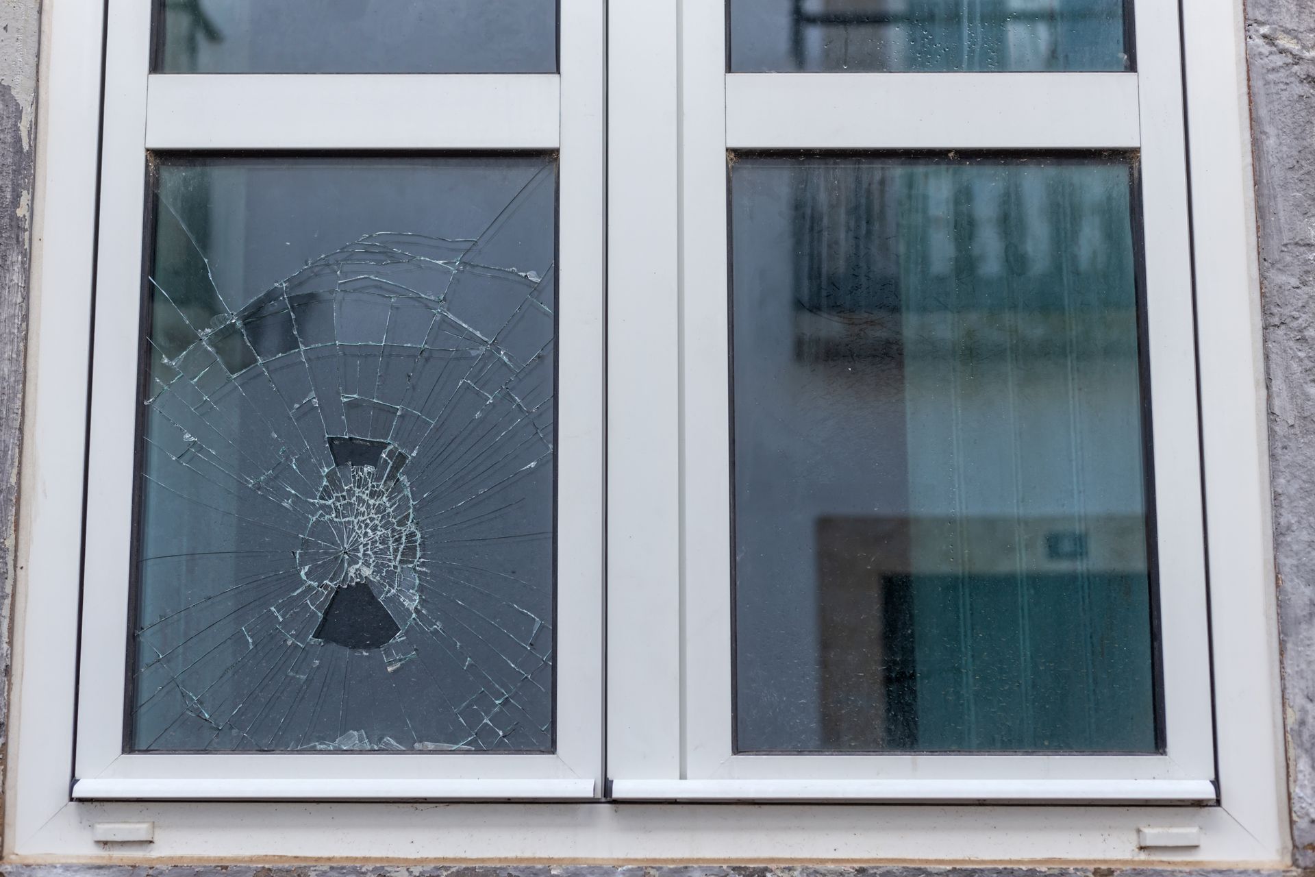 Window with cracked glass, light frame, and reflection of a building facade.