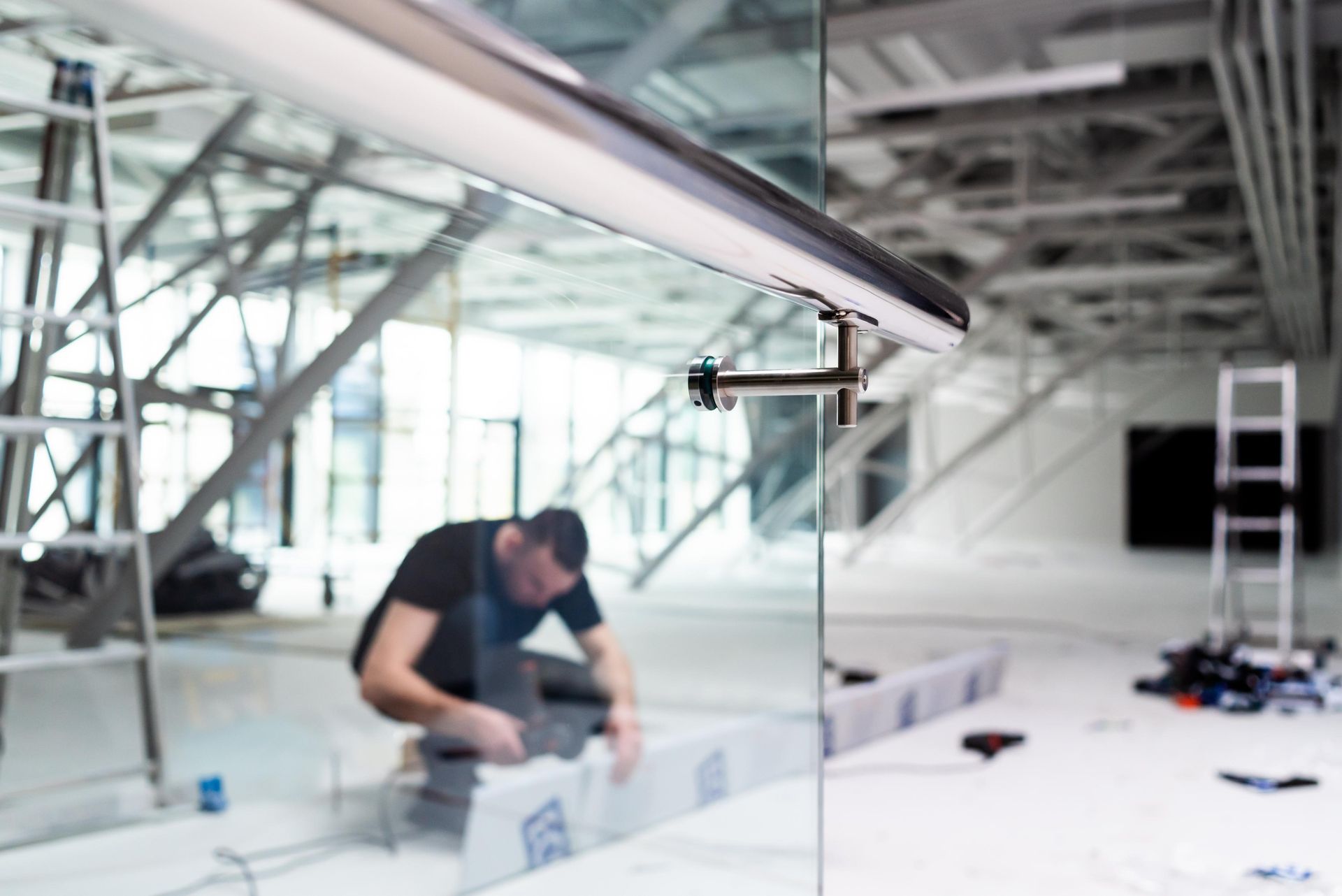 A construction worker installs a glass panel with a metal handrail in a modern building.