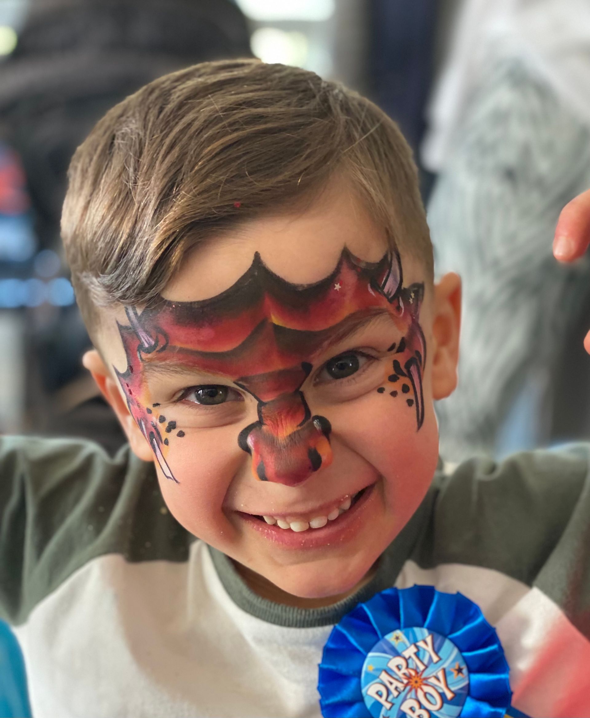 Boy with dragon face paint smiles, wearing a blue 