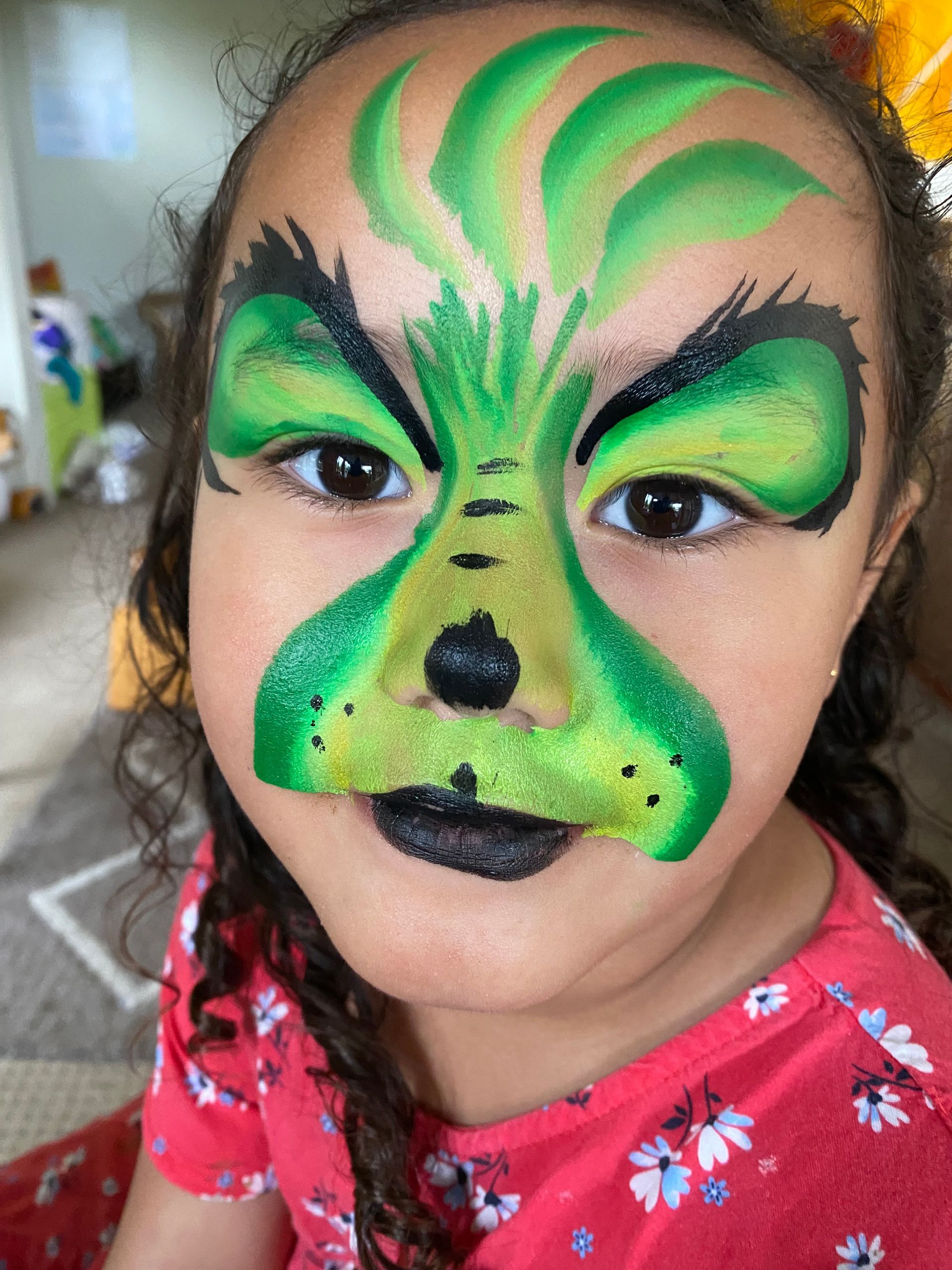 Child with Grinch face paint; green and black, smiling slightly.