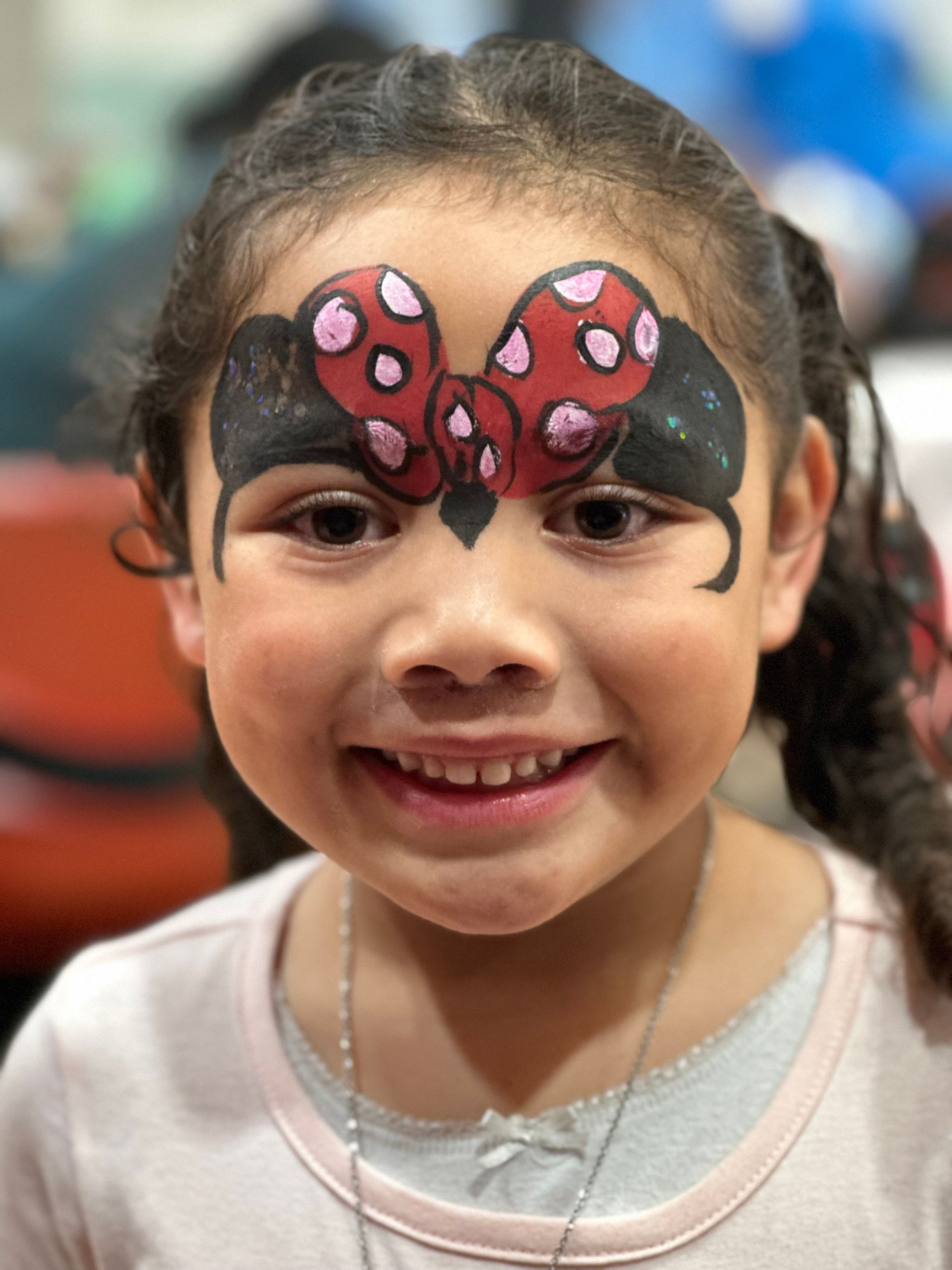 Girl with Minnie Mouse face paint smiles at the camera.