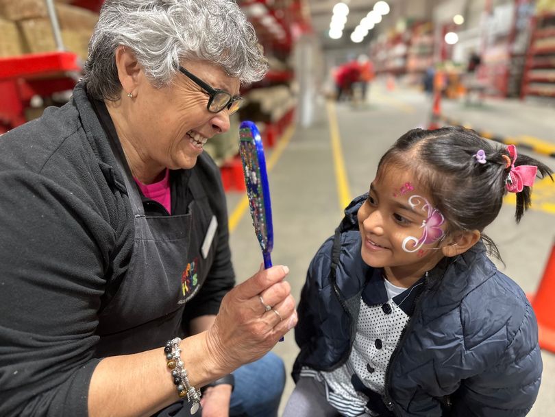 Woman showing a child her face paint in a hardware store; both are smiling.