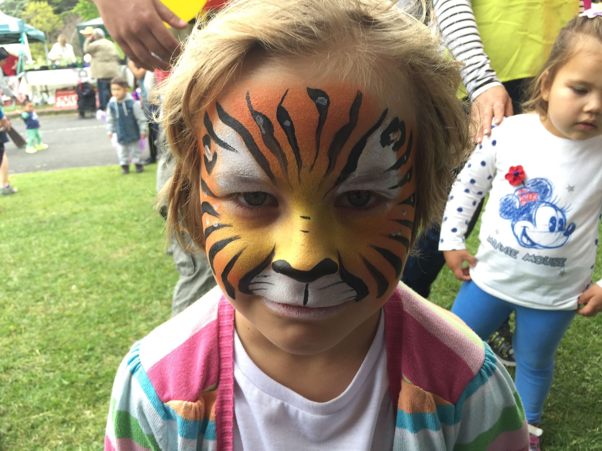 Girl with tiger face paint at outdoor event.