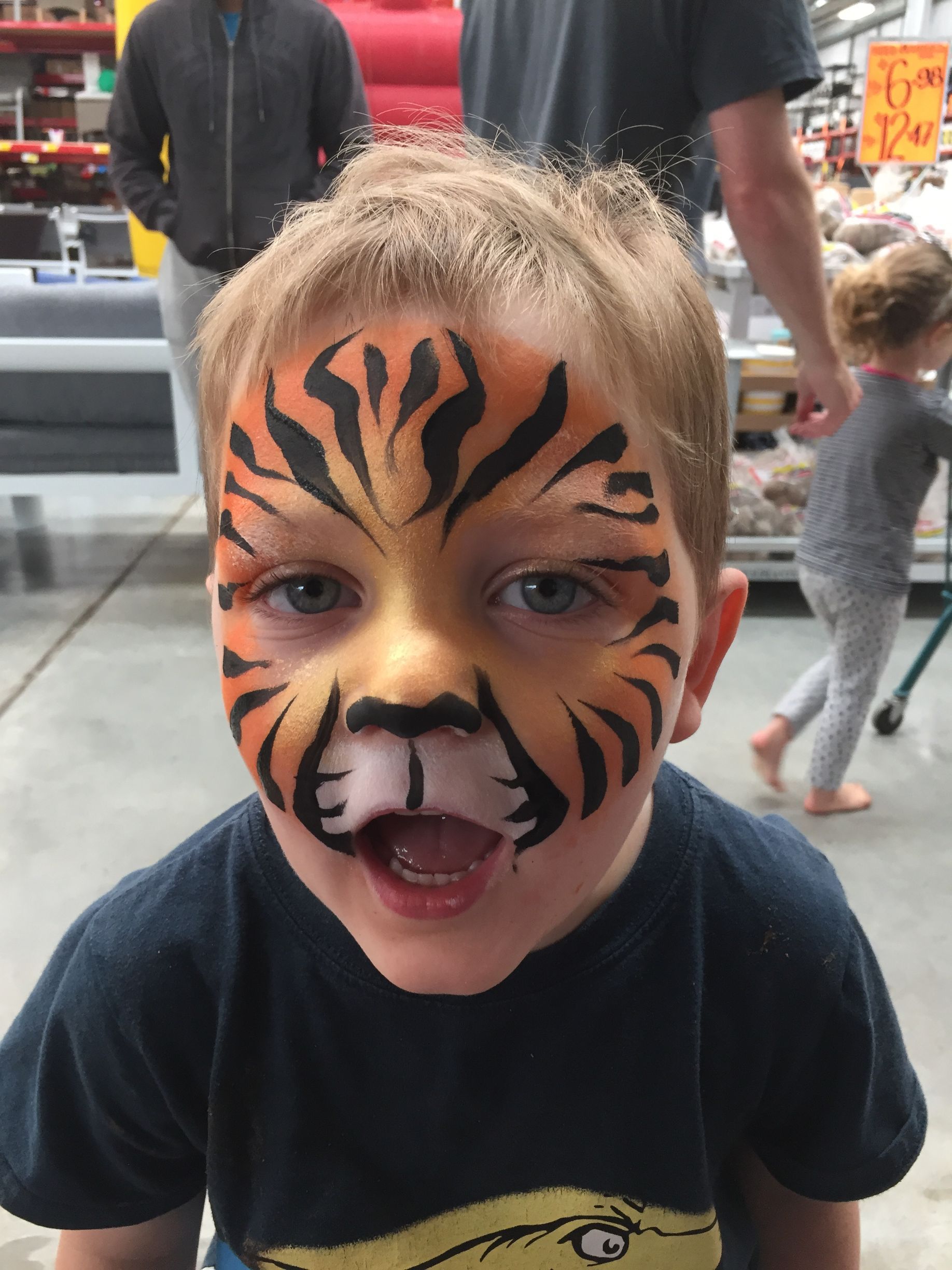 Boy with tiger face paint smiling, inside a store.