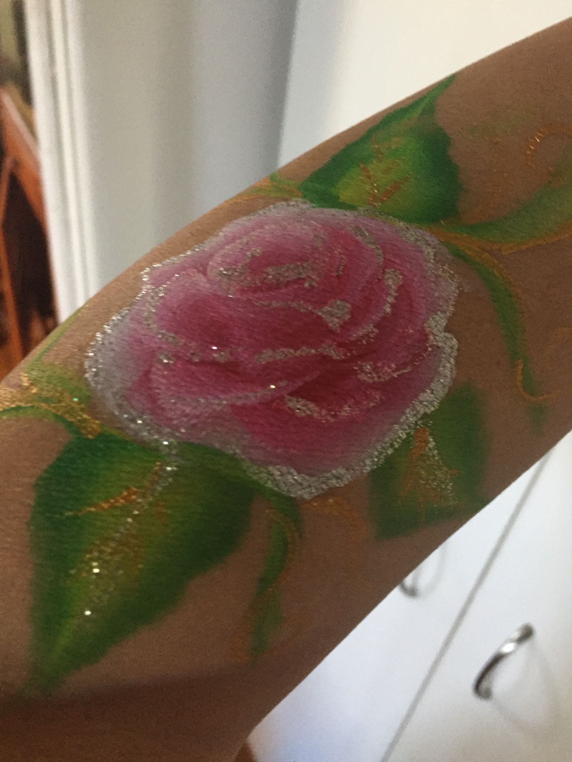Pink rose body paint with glitter, green leaves, and stem on an arm.