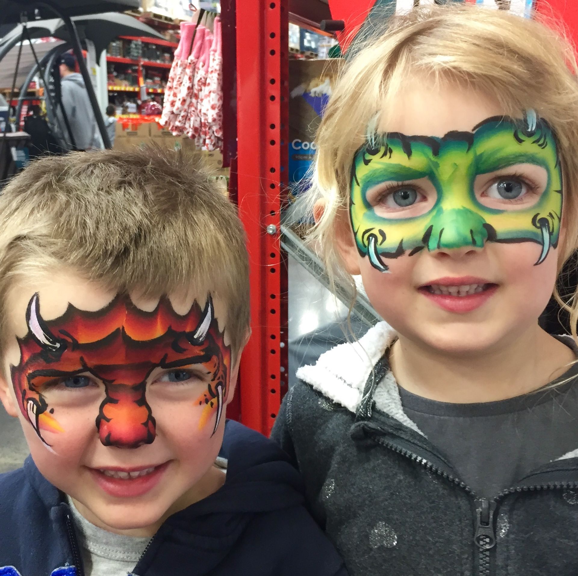 Two children with dragon face paint smiling indoors.