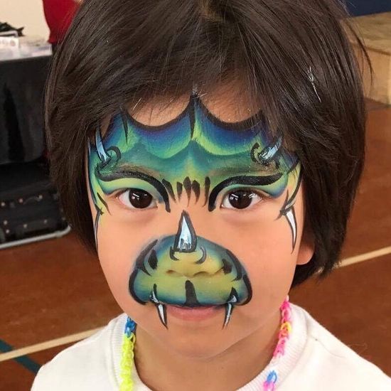 A child with dragon face paint: green, blue, and black scales and fangs.