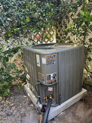 A large air conditioner is sitting on top of a concrete platform in a backyard.