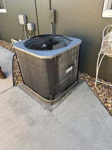 An air conditioner is sitting on the sidewalk next to a house.