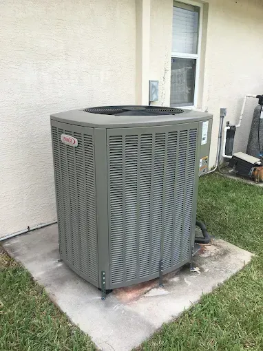 A large air conditioner is sitting on top of a concrete slab in the backyard of a house.