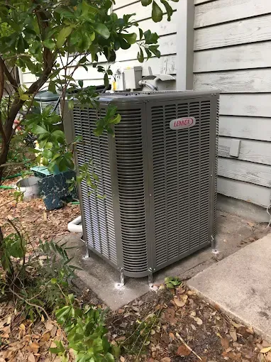 An air conditioner is sitting on the side of a house next to a tree.